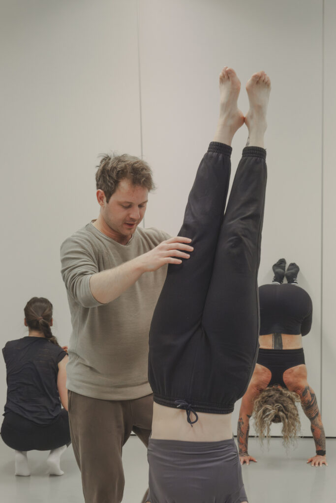 Marius corrects a student’s alignment in a handstand