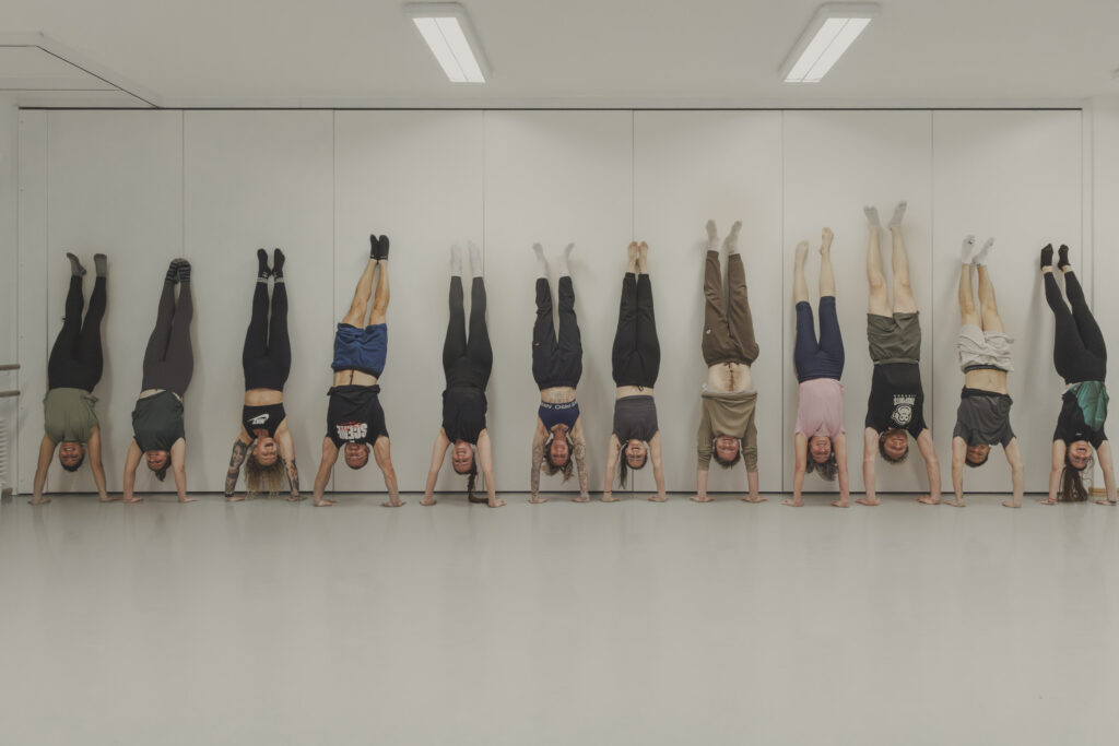 Twelve students in a handstand against the wall during a weekly class