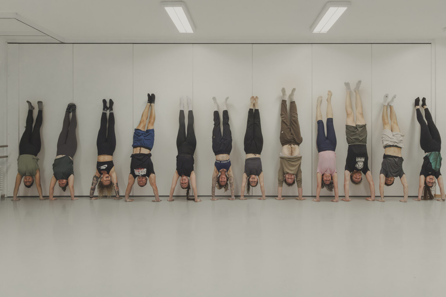 Zwölf Teilnehmende im Handstand an der Wand während des Kurses